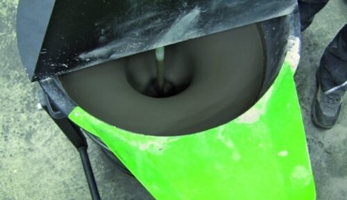 A close-up view of a mixing drum with a dark, paste-like substance being mixed inside. The drum has a green lid and is mounted on a stand.